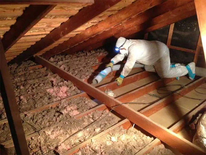 Technician in a protective suit treating attic insulation