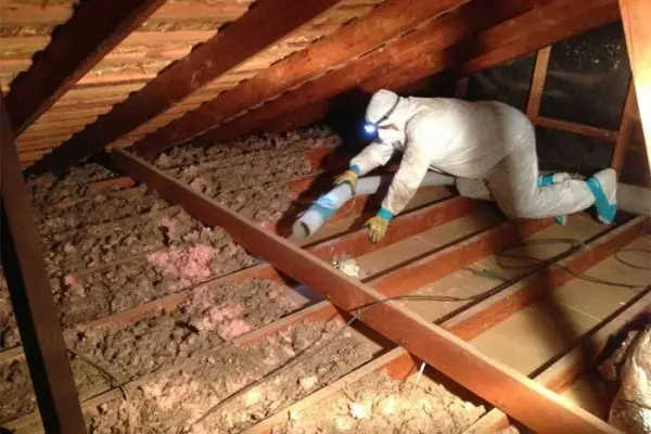 Technician in a protective suit treating attic insulation