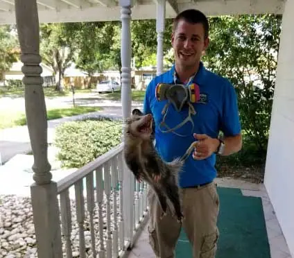 Pro Wildlife Removal technician holding a captured animal on a porch